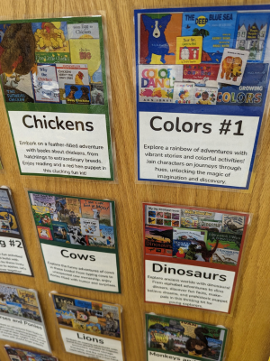 Image of a wall with notecards listing offerings for Youth Reading Kits. This image is zoomed in on a kit about Chickens, one about Colors, one about Cows, and one about Dinosaurs.